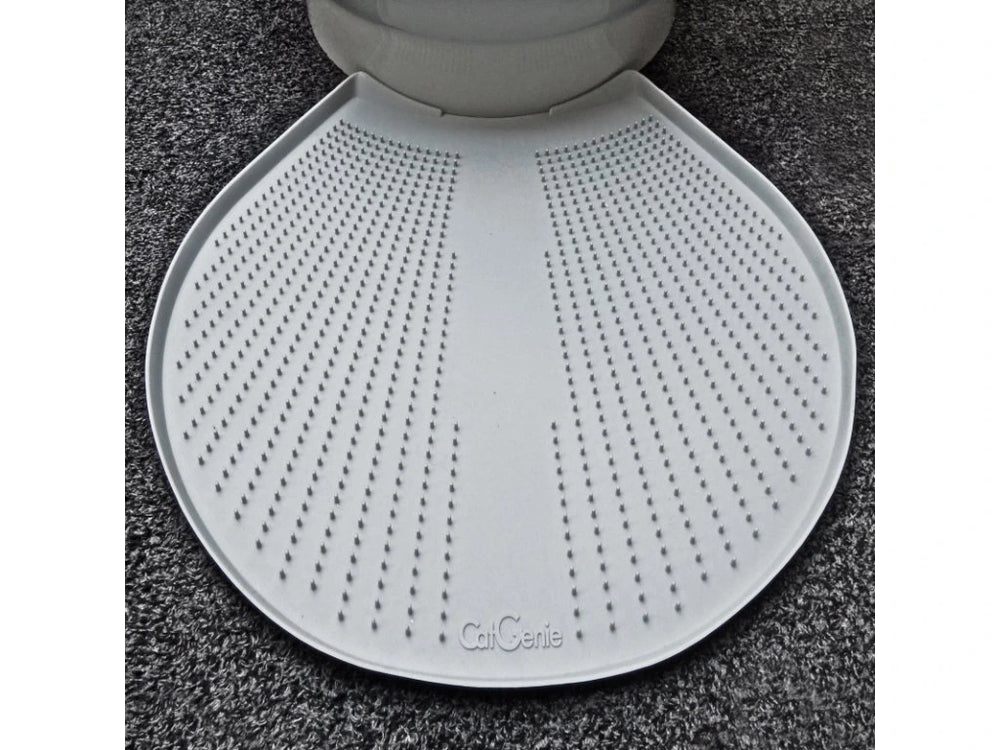 Eine weiße, strukturierte CatGenie GenieMat sitzt vor einem Katzenklo auf einem dunklen Teppichboden. Sie wurde entwickelt, um streunendes CatGenie Granulat aufzufangen und Ihren Raum sauber zu halten.