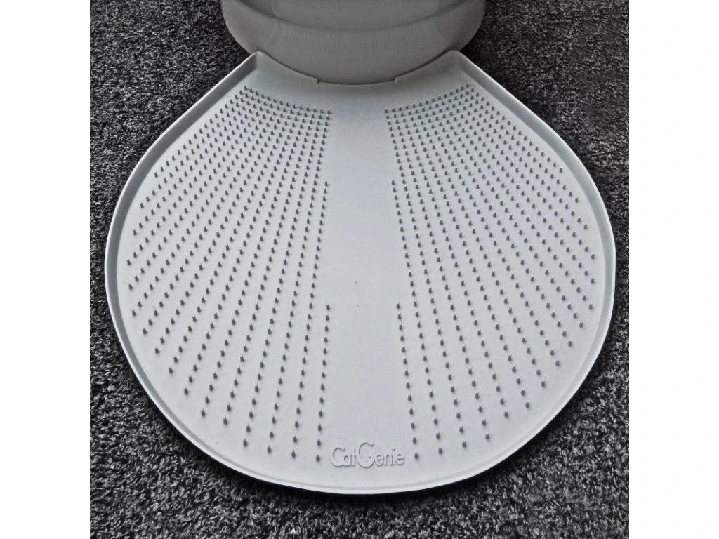 Eine weiße, strukturierte CatGenie GenieMat sitzt vor einem Katzenklo auf einem dunklen Teppichboden. Sie wurde entwickelt, um streunendes CatGenie Granulat aufzufangen und Ihren Raum sauber zu halten.